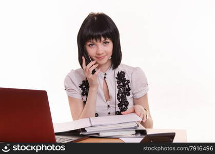 Cute little girl sitting at a table in a call center with a laptop in a white blouse with a phone in his hand. Office employee call-center with phone in hand