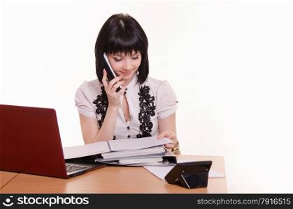 Cute little girl sitting at a table in a call center with a laptop in a white blouse with a phone in his hand