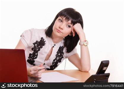 Cute little girl sitting at a table in the call center with laptop in white blouse propped his head on his hand. Thoughtful call-center employee leaned her head on