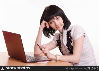Cute little girl sitting at a table in the call center with laptop in white blouse. Call-center employee at desk rests his head on