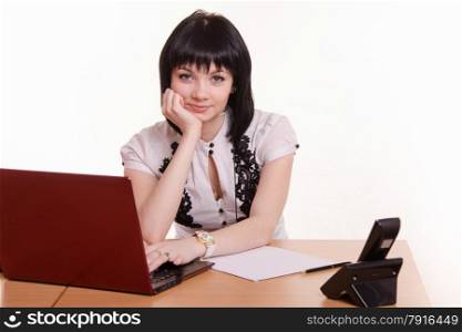 Cute little girl sitting at a table in the call center with laptop in white blouse propped his head on his hand. Office employee call-center leaned her head