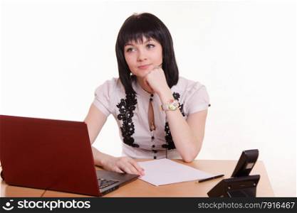 Cute little girl sitting at a table in the call center with laptop in white blouse propped his head on his hand. Dreamy office employee call-center leaned on the arm