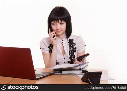 Cute little girl sitting at a table in the call center with laptop in white blouse. Call-center worker talking on the phone
