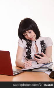 Cute little girl sitting at a table in the call center with laptop in white blouse. Call-center worker at desk with a phone