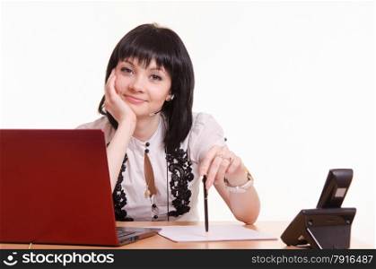 Cute little girl sitting at a table in the call center with laptop in white blouse propped his head on his hand. Call-center employee at a desk with pen in hand