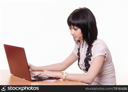 Cute little girl sitting at a table in the call center with laptop in white blouse. Call-center employee at the desk