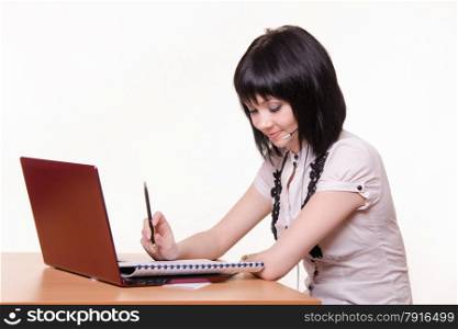 Cute little girl sitting at a table in the call center with laptop in white blouse. Girl - call-center employee at the desk with documents