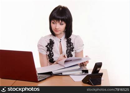 Cute little girl sitting at a table in the call center with laptop in white blouse with documents in hand. Office employee call-center verifies information in the computer and documents
