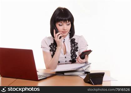 Cute little girl sitting at a table in the call center with laptop in white blouse. Call-center worker talking on phone and looking at the other