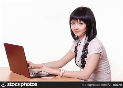 Cute little girl sitting at a table in the call center with laptop in white blouse. Call-center employee at a table with laptop