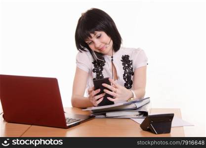Cute little girl sitting at a table in the call center with laptop in white blouse. Call-center worker with phone and a pile of papers