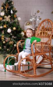 cute little girl sitting in rocking chair near christmas tree.. cute little girl sitting in rocking chair near christmas tree