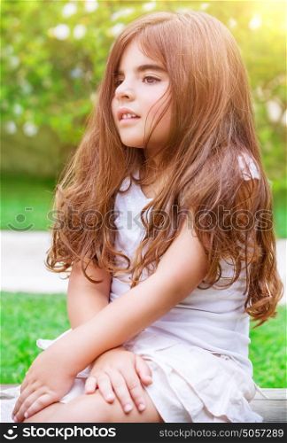 Cute little girl sitting on backyard in bright sunny day, spending summer holidays in summer camp, happy healthy childhood