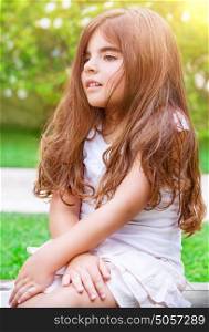 Cute little girl sitting on backyard in bright sunny day, spending summer holidays in summer camp, happy healthy childhood