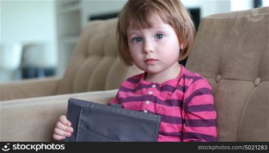 Cute little girl sitting on coutch and using touchpad or tablet and smiling