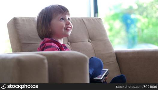 Cute little girl sitting on coutch and using touchpad or tablet and smiling