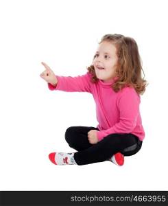 Cute little girl sitting on the floor pointing something with the finger isolated on a white background