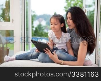 Cute little girl sitting with her mother on couch using a digital tablet
