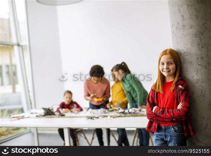 Cute little girl standing in front of  group of kids programming electric toys and robots at robotics classroom
