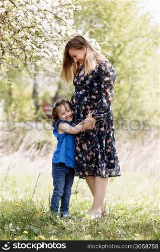 Cute little girl touching her mother&rsquo;s pregnant belly in summer nature.. pregnant mother with daughter in nature. Cute little girl touching her mother&rsquo;s pregnant belly in summer nature