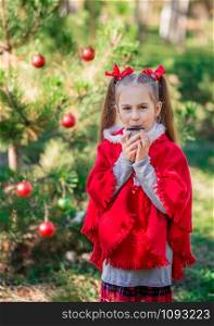 Cute little girl warms herself with a cup of hot drink in the forest against the background of the Christmas tree. Winter holidays and people concept. Merry Christmas and happy holidays.. Cute little girl warms herself with a cup of hot drink in the forest against the background of the Christmas tree.