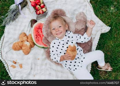 cute little girl with croissant lying on blanket on picnic. happy summer holiday. Concept of childhood and tenderness.. cute little girl with croissant lying on blanket on picnic. happy summer holiday. Concept of childhood and tenderness