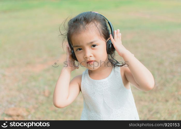 cute little girl with headphone for listening in the park, her face feel like happy with sunshine. subject is blurry.