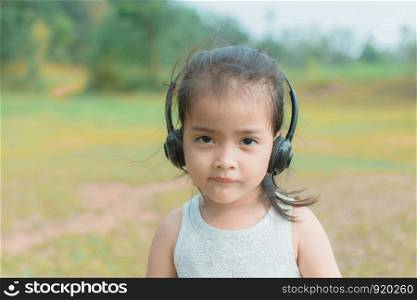 cute little girl with headphone for listening in the park, her face feel like happy with sunshine. subject is blurry.