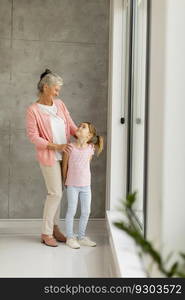 Cute little girl with her grandmother standing by the window