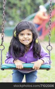 Cute little girl with her hair on her face, posing on a swing