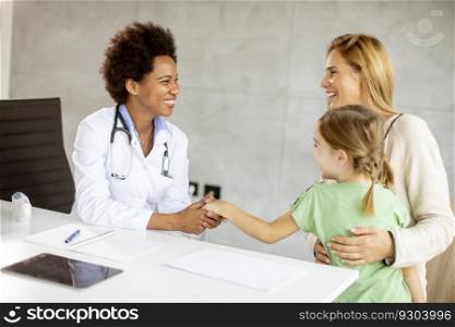 Cute little girl with her mother at the pediatrician examination by African american female doctor