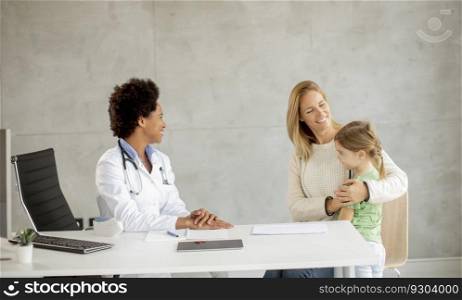 Cute little girl with her mother at the pediatrician examination by African american female doctor