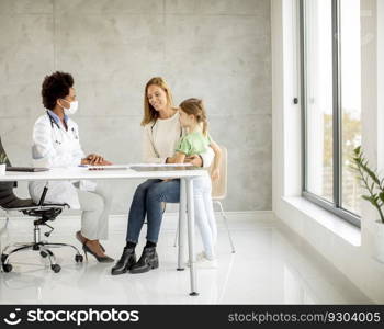 Cute little girl with her mother at the pediatrician examination by African american female doctor