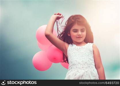 Cute little girl with pink air balloons over blue sky background, enjoying birthday party, happy carefree childhood . Happy girl with air balloons