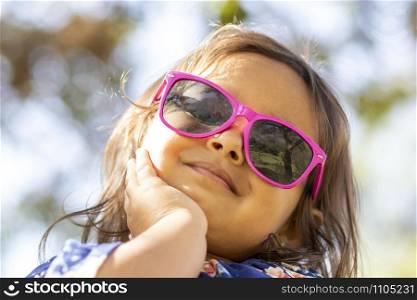 Cute little girl with pink sunglasses and hands on her face.