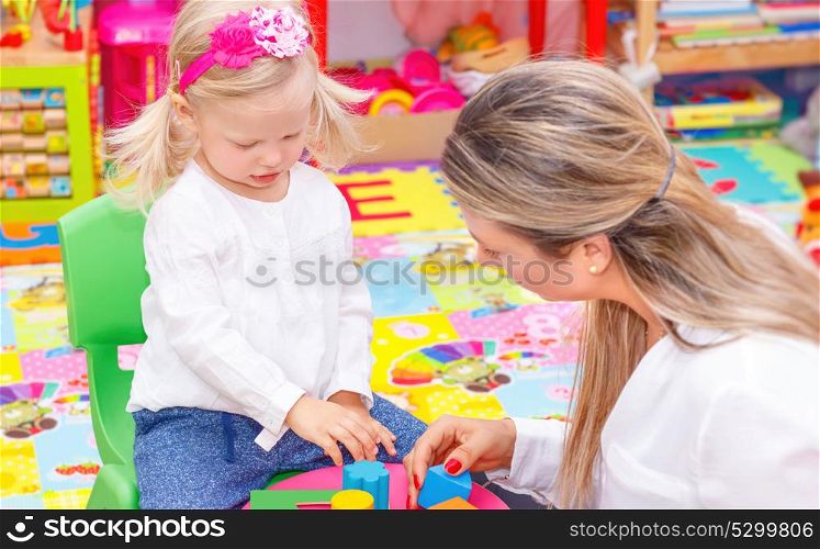 Cute little girl with young beautiful mother playing game in colorful playroom, happy family with pleasure spending time together