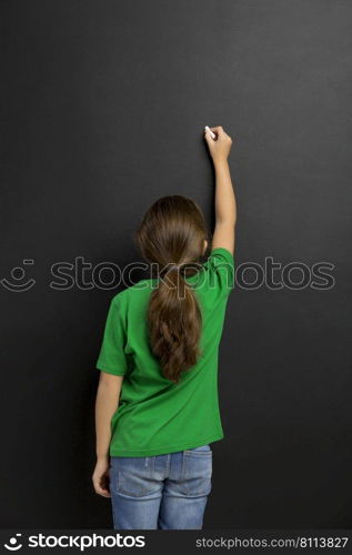 Cute little girl writing in a blackboard, with copy space.