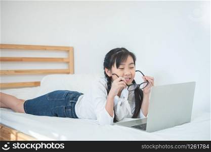 Cute little happy asian girl smile lying on bed in bedroom at home playing game online on laptop.