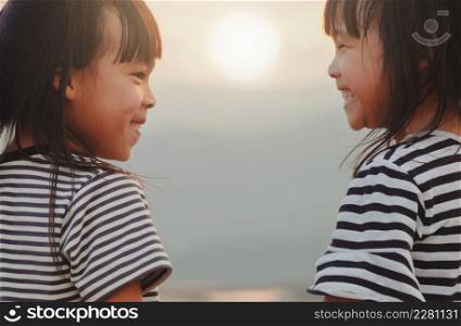 Cute little sisters looking at each other and smiling against the sunset background. The concept of family and sibling love