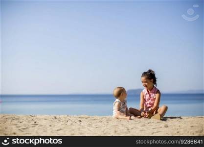 Cute little sisters sitting on a beach at summer