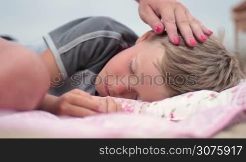 Cute little son fell asleep on picnic. Mother caressing her boy with tenderness.