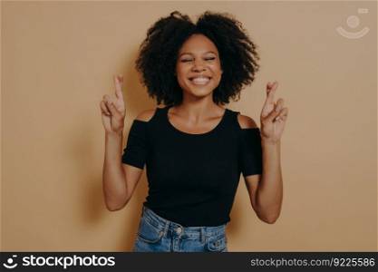 Cute lovely african american woman posing in casual clothes while gesturing fingers crossed sign, smiling with hope and eyes closed. Luck, superstitious and body language concept. Cute lovely african american woman posing in casual clothes while gesturing fingers crossed sign