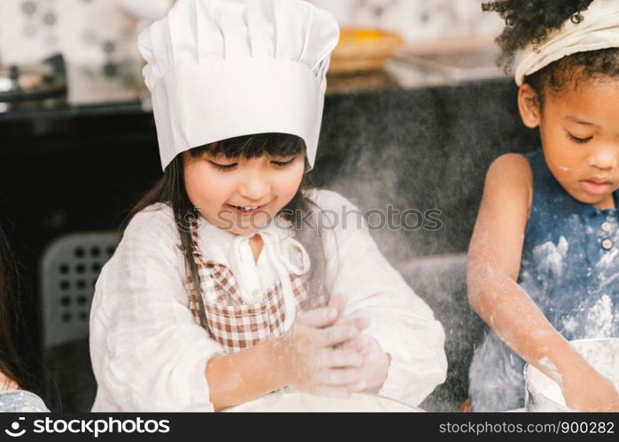 Cute mixed race and African American kid girls baking or cooking together in home kitchen. Education activity, youth culture, or smart young children concept