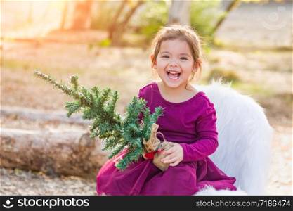 Cute Mixed Race Young Baby Girl Holding Small Christmas Tree Outdoors.