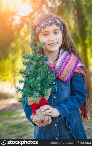 Cute Mixed Race Young Girl Holding Small Christmas Tree Outdoors.