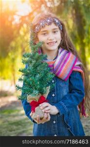 Cute Mixed Race Young Girl Holding Small Christmas Tree Outdoors.