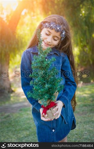 Cute Mixed Race Young Girl Holding Small Christmas Tree Outdoors.