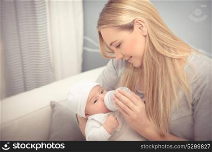 Cute mother feeding her adorable newborn baby in the beautiful cozy kid&rsquo;s room at home, healthy milk nutrition for infants, enjoying parenthood, happy family life