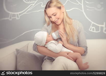 Cute mother feeding her adorable newborn baby in the beautiful cozy kid&rsquo;s room at home, special milk formula for infants, enjoying parenthood, happy family life