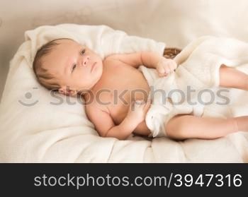 Cute naked caucasian baby boy lying under blanket on bed
